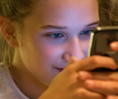 A teenage girl looks closely at her smartphone in a dimly lit room