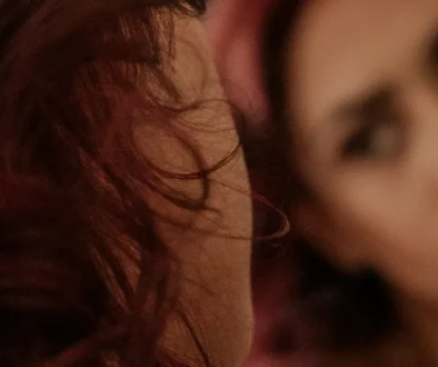 A woman with dark red hair looks at her blurred reflection in a mirror