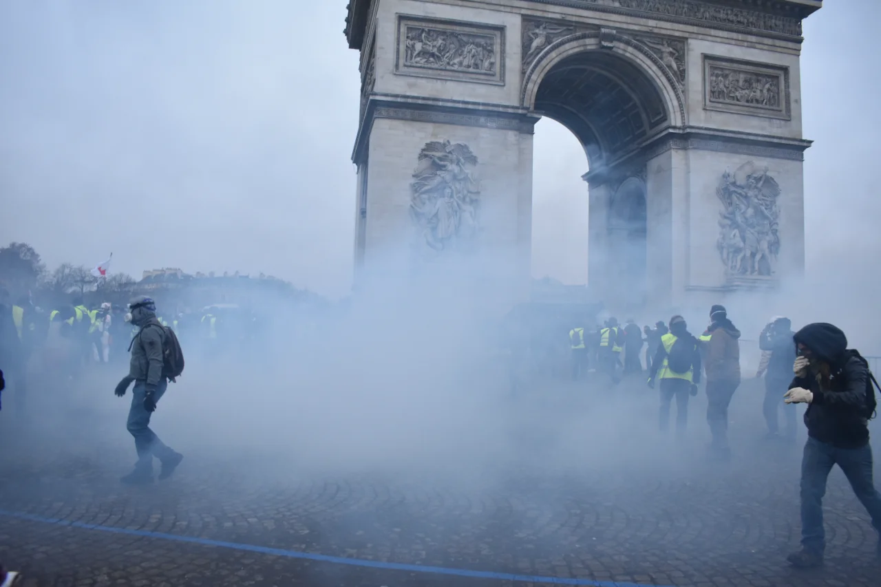 Protesters walk through thick tear gas in front of the Arc de Triomphe in Paris, some covering their faces